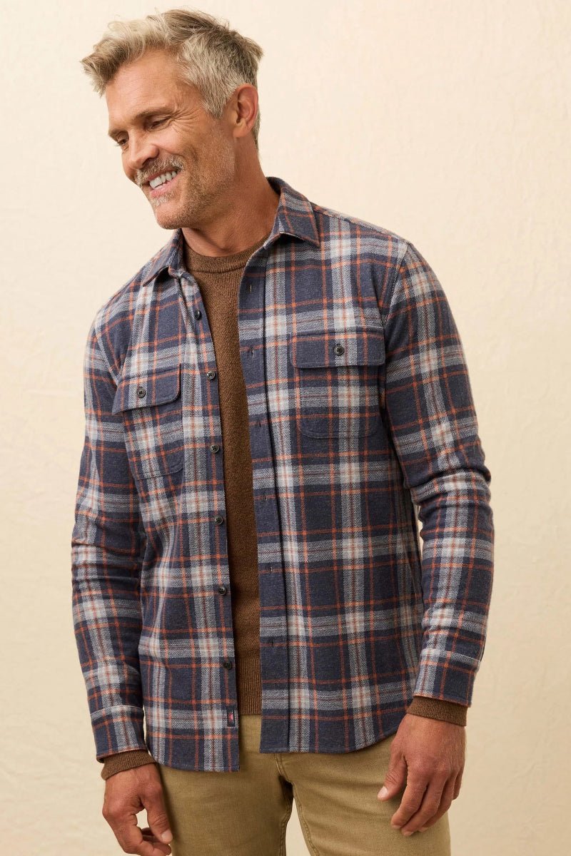 Man wearing a plaid shirt over a brown sweater on a beige background