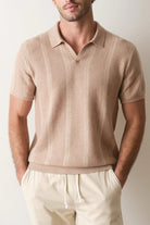 Man wearing a beige polo shirt and pants against a plain background
