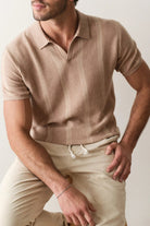 Man wearing a beige polo shirt and pants against a plain background
