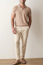 Man wearing a beige polo shirt and pants standing against a plain background