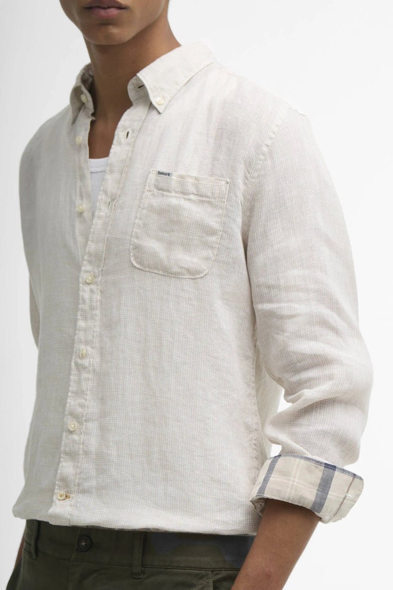 Man wearing a light-colored button-up shirt with rolled-up sleeves on a plain background