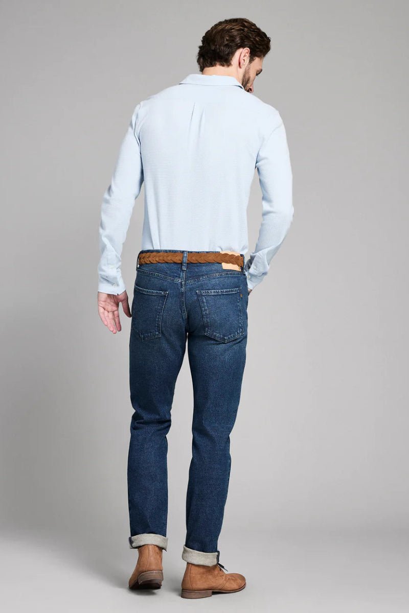 Man wearing a light blue shirt and dark blue jeans on a gray background
