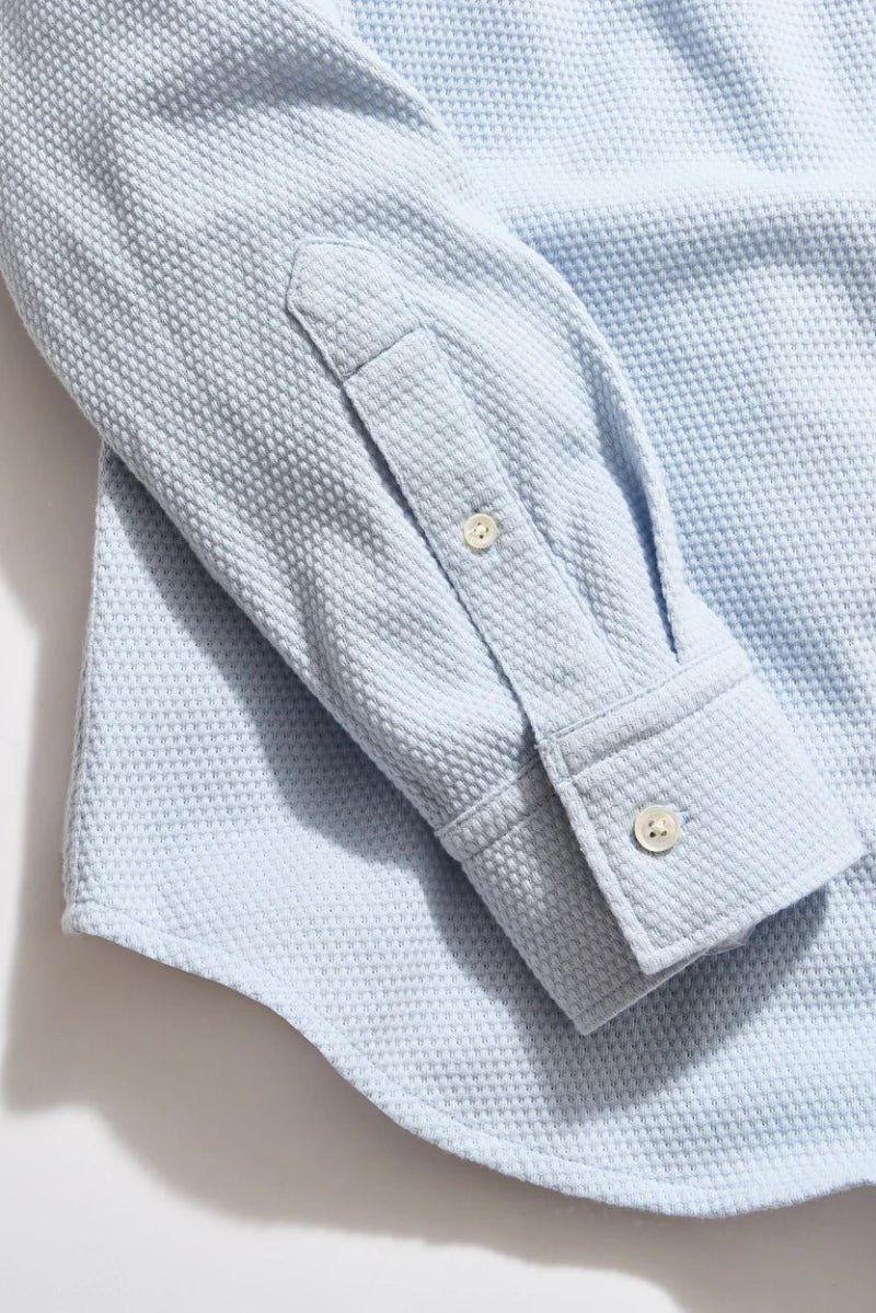 Light blue textured shirt with rolled-up sleeve on a neutral background