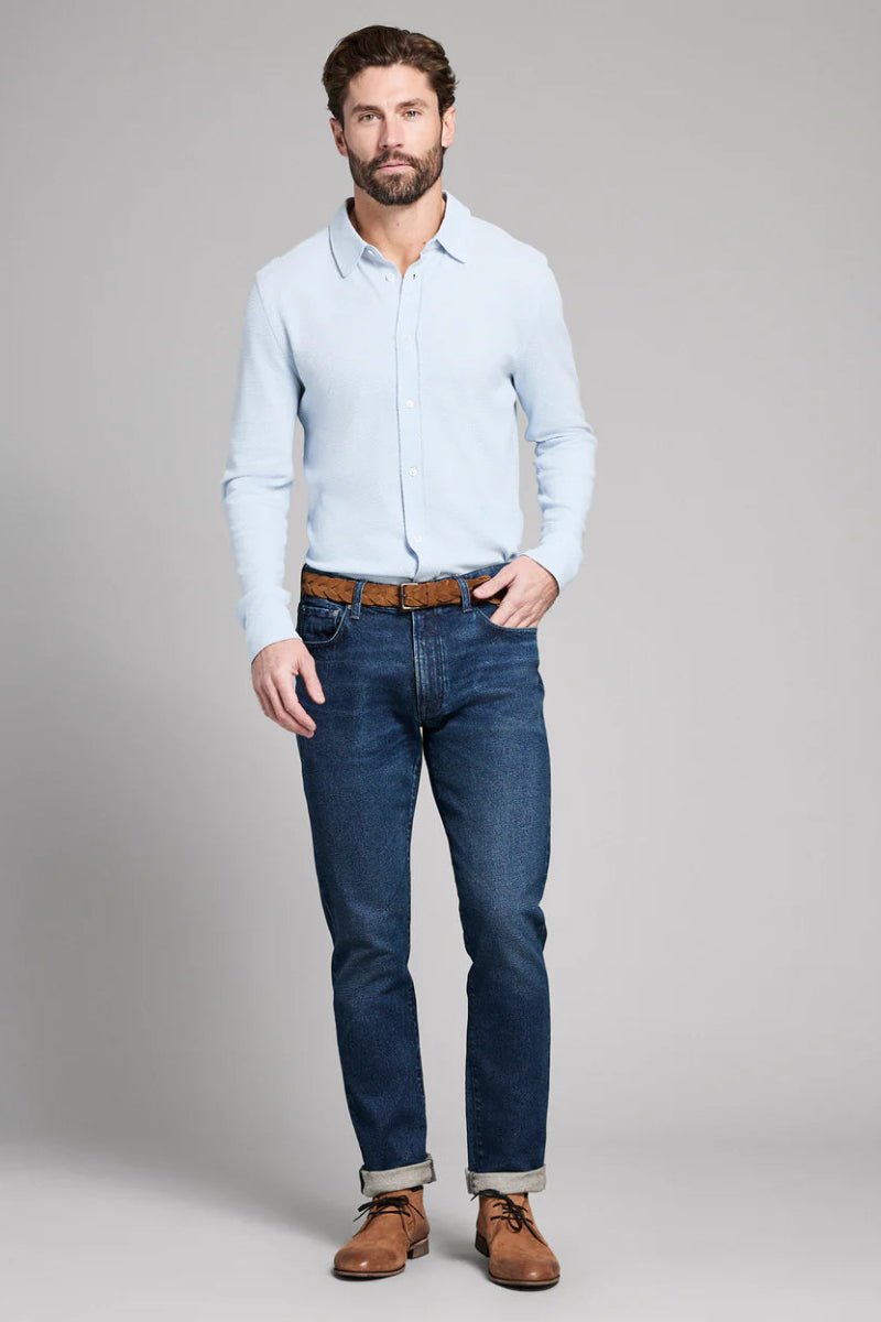 Man wearing a light blue shirt, dark blue jeans, and brown shoes on a gray background