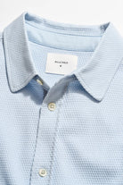 Light blue textured polo shirt with a brand label on a light gray background