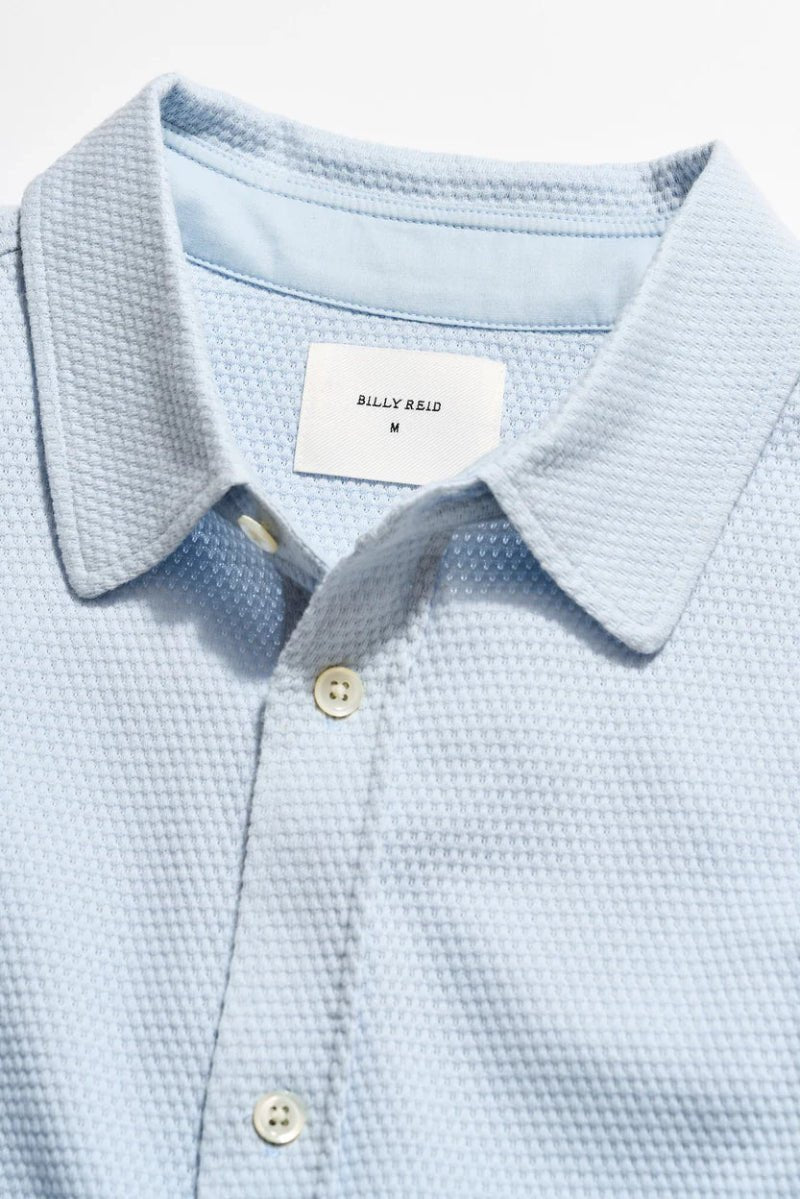Light blue textured polo shirt with a brand label on a light gray background