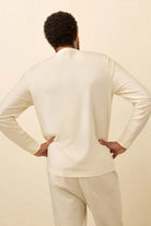 Person wearing a cream-colored long-sleeve top and pants against a beige background