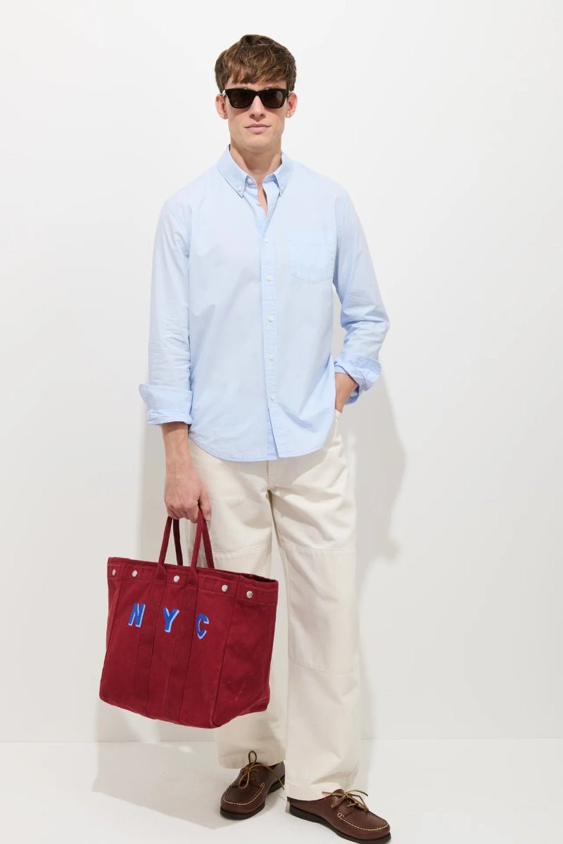 Man holding a red tote bag with 'NYC' letters against a white background