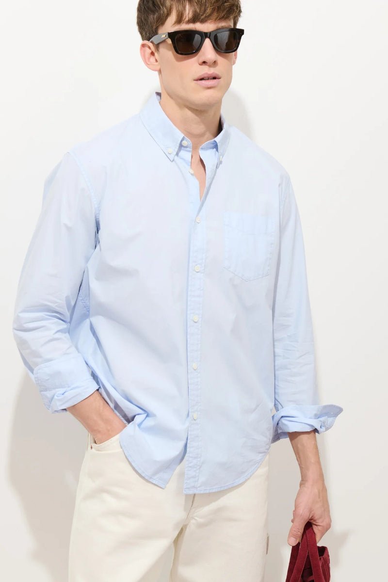 Man wearing a light blue shirt and sunglasses against a white background