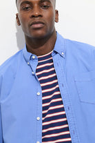 Man wearing a blue shirt over a striped shirt against a white background