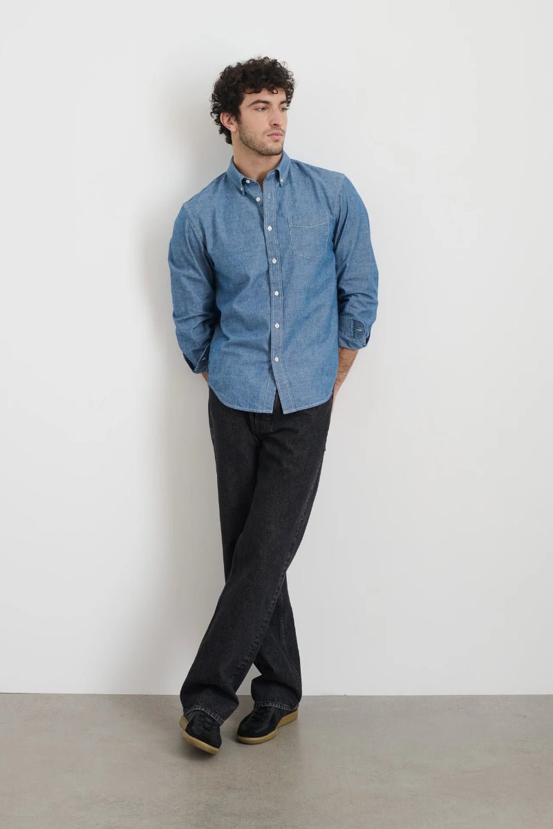 Man wearing a blue shirt and black pants against a white background