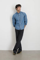 Man wearing a blue shirt and black pants against a white background