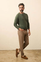 Man wearing a green sweater and brown pants standing against a plain background