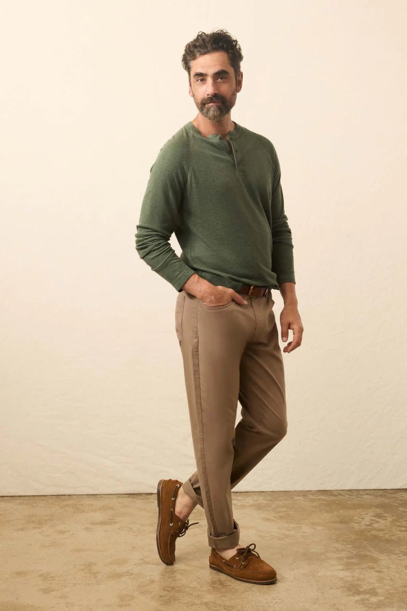 Man wearing a green sweater and brown pants standing against a plain background