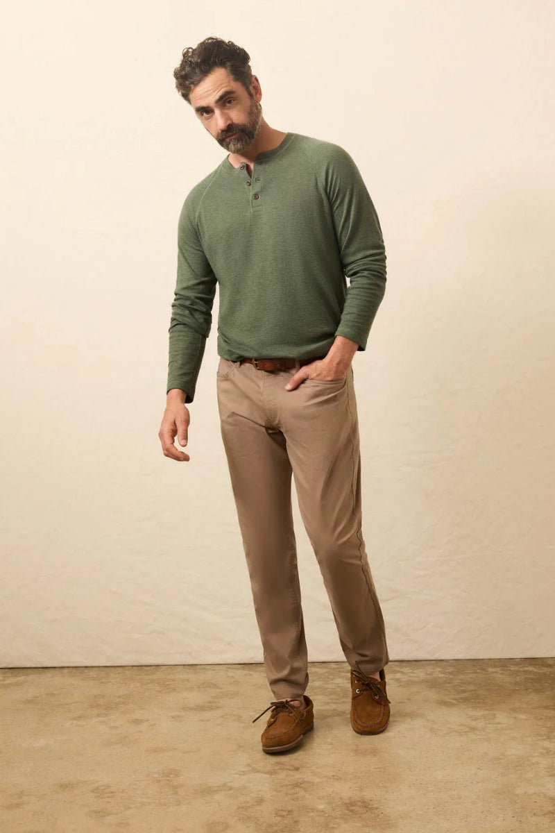 Man wearing a green sweater and brown pants standing against a plain background