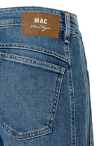 Close-up of blue jeans with a 'MAC vintage' label on a white background