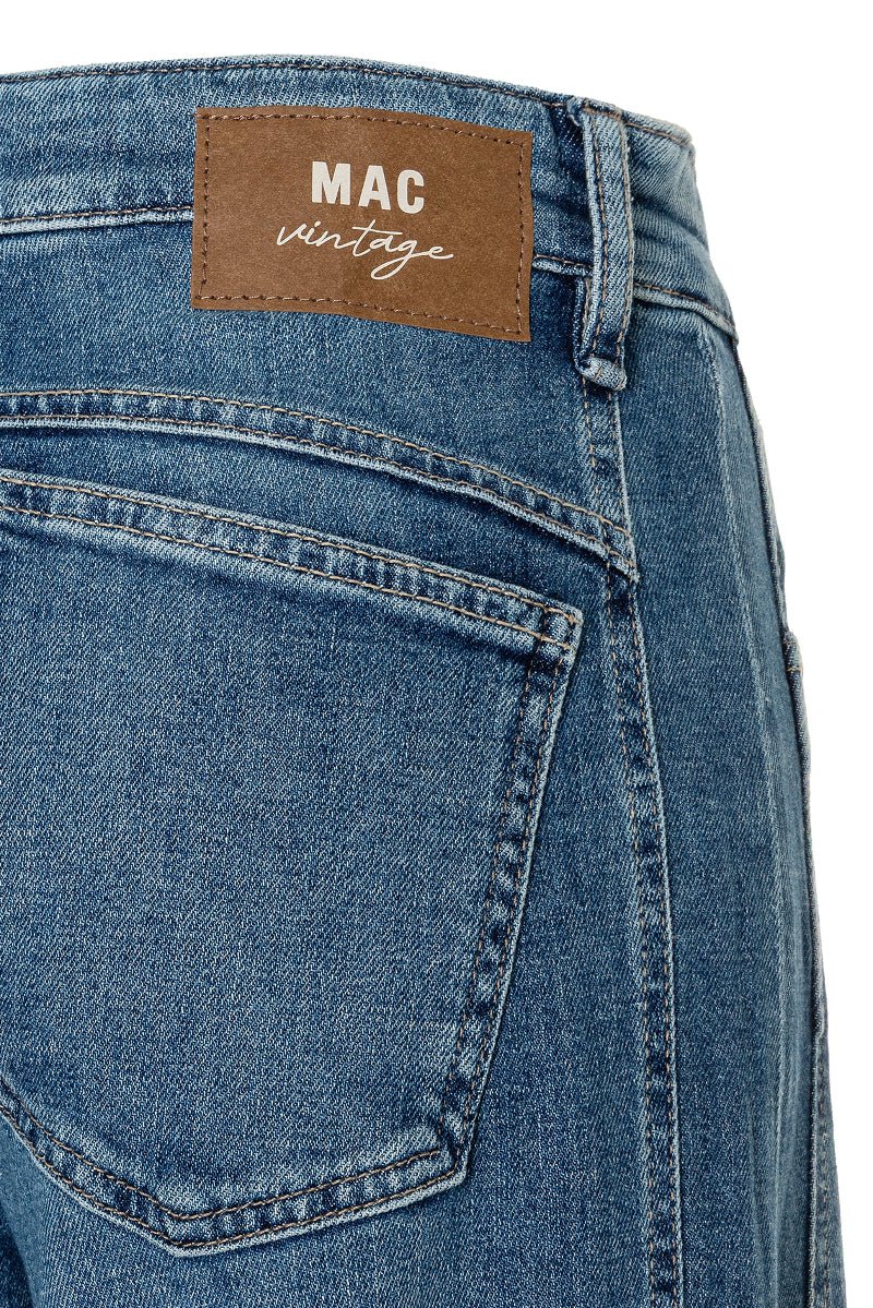 Close-up of blue jeans with a 'MAC vintage' label on a white background