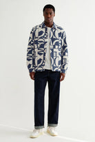 Man wearing a patterned shirt and dark jeans on a white background