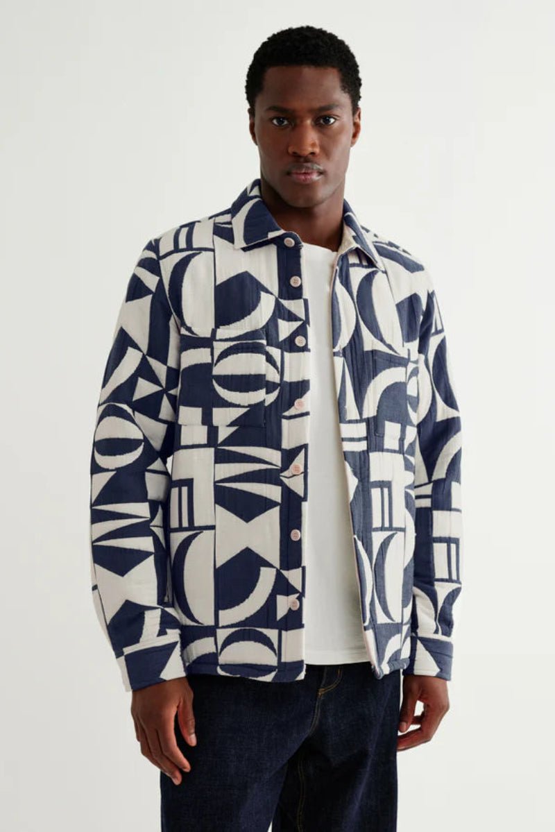 Man wearing a patterned shirt over a plain shirt on a white background