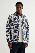 Man wearing a patterned shirt over a plain shirt on a white background