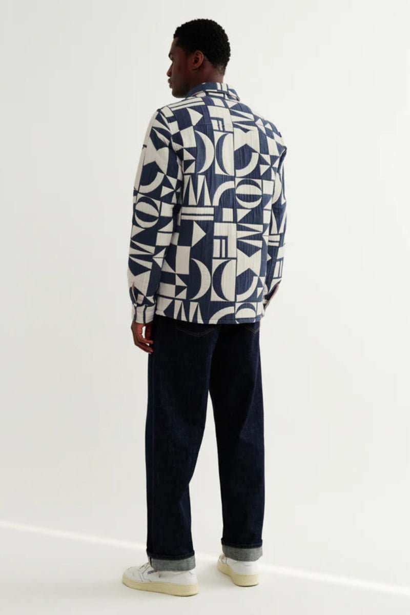 Person wearing a patterned sweater and dark pants on a white background