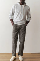 Person wearing a gray hoodie and dark pants standing against a plain white wall.