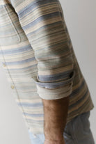 Close-up of a person wearing a striped shirt with rolled-up sleeves against a neutral background