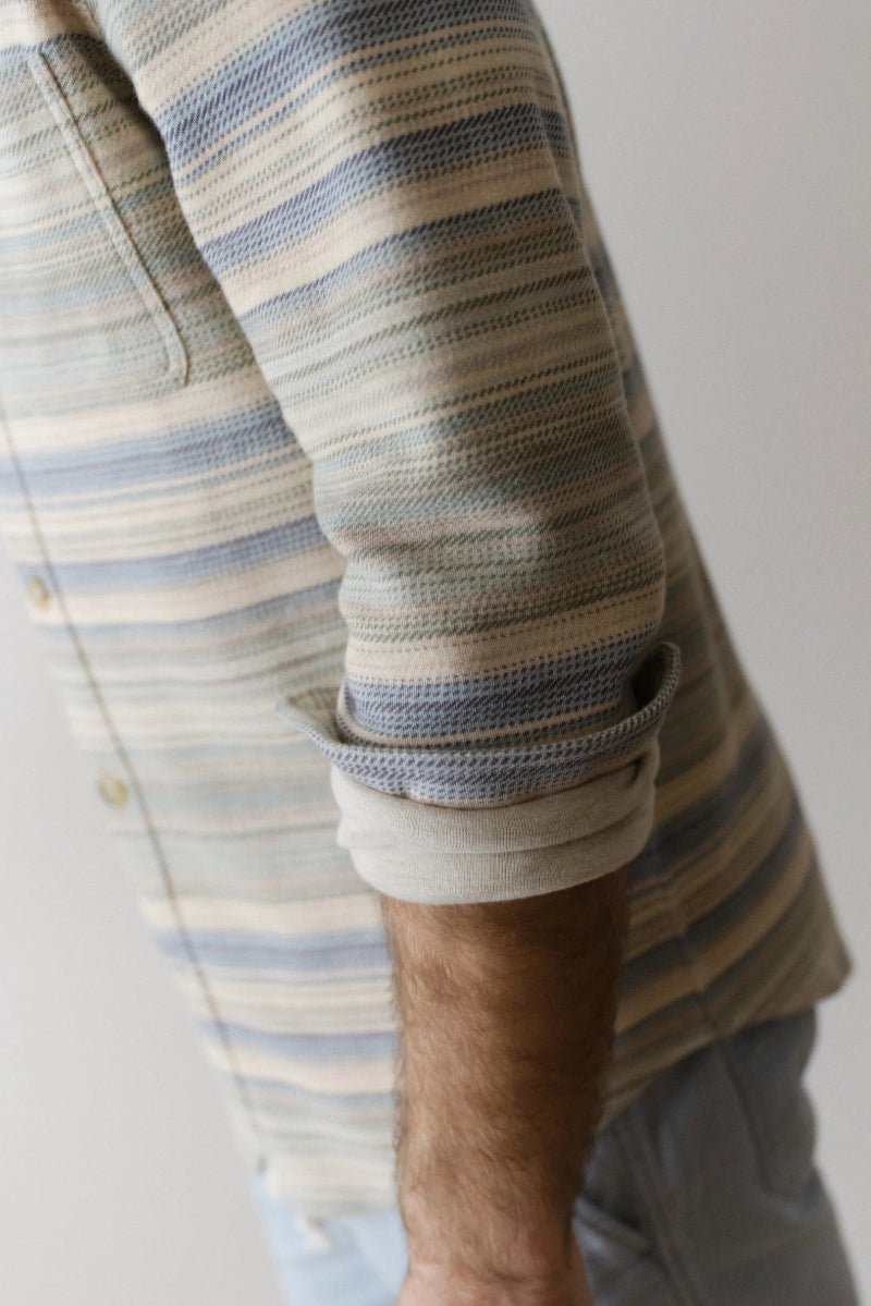 Close-up of a person wearing a striped shirt with rolled-up sleeves against a neutral background