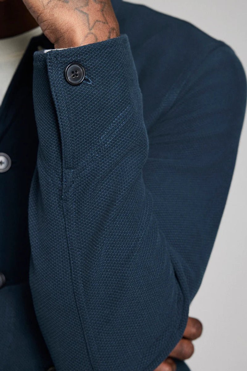 Close-up of a person wearing a dark blue textured coat with buttons on a neutral background