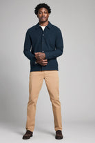 Man wearing a navy jacket and beige pants on a gray background