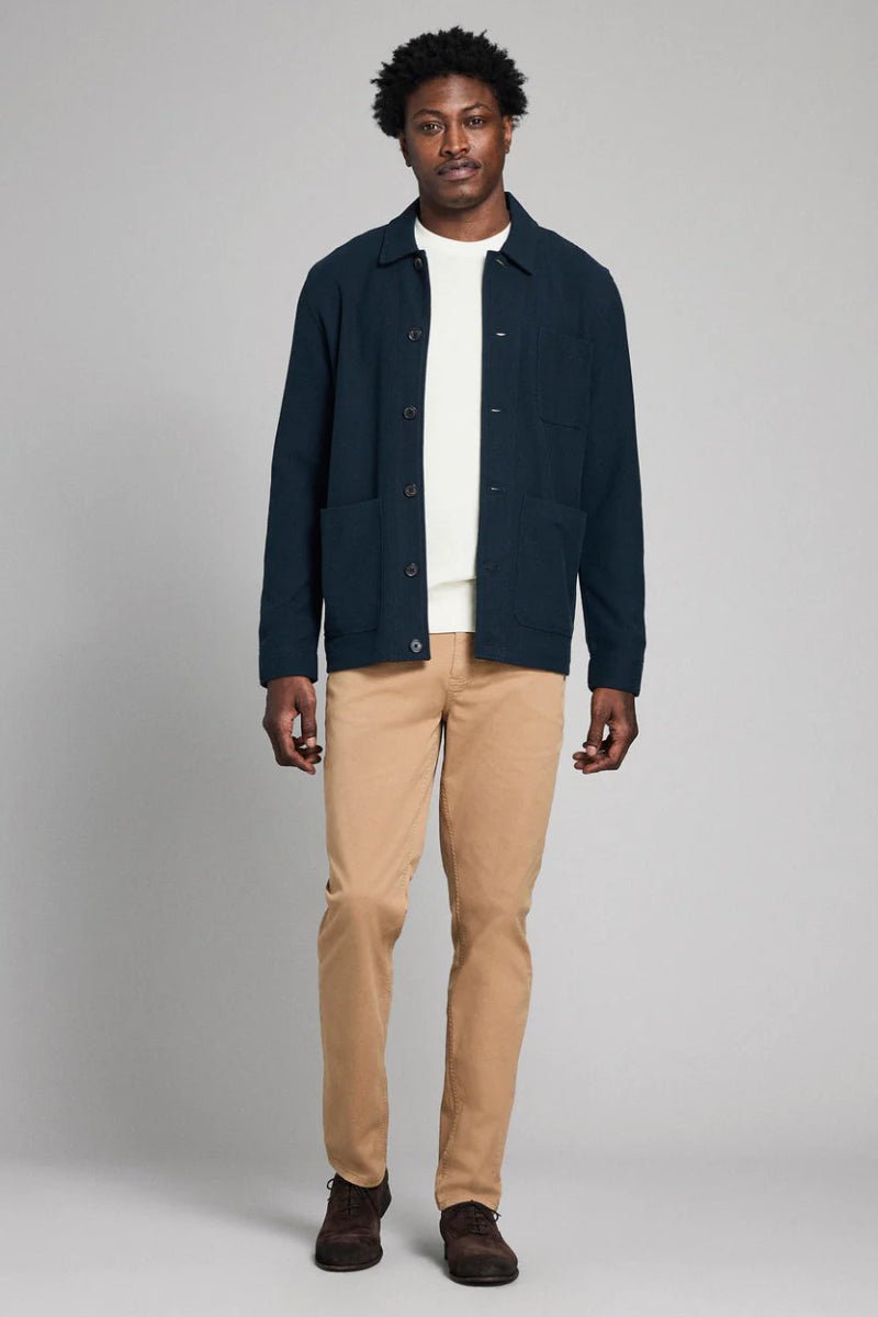 Man wearing a navy jacket, white shirt, beige pants, and brown shoes on a gray background