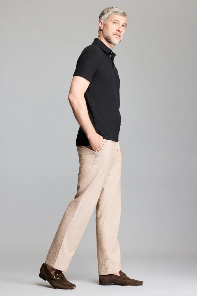 Man wearing a black polo shirt and beige pants on a gray background