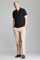 Man wearing a black polo shirt and beige pants on a gray background