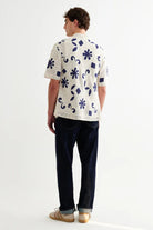 Person wearing a white shirt with blue floral patterns and dark pants on a white background