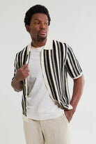 Man wearing a black and white striped shirt over a white t-shirt on a plain background