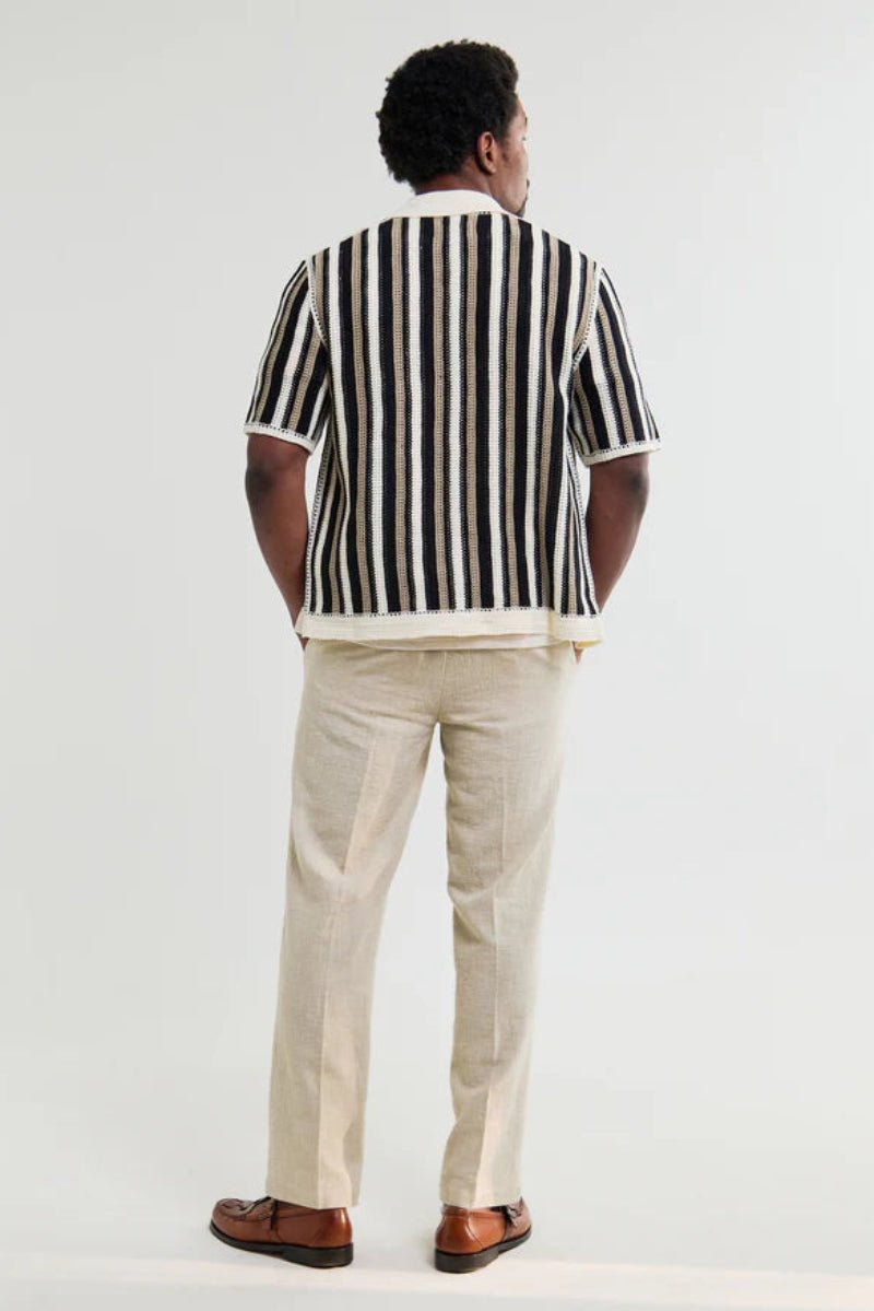 Person wearing a black and white striped shirt and beige pants on a white background