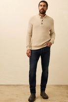 Man wearing a beige sweater and dark jeans against a plain background