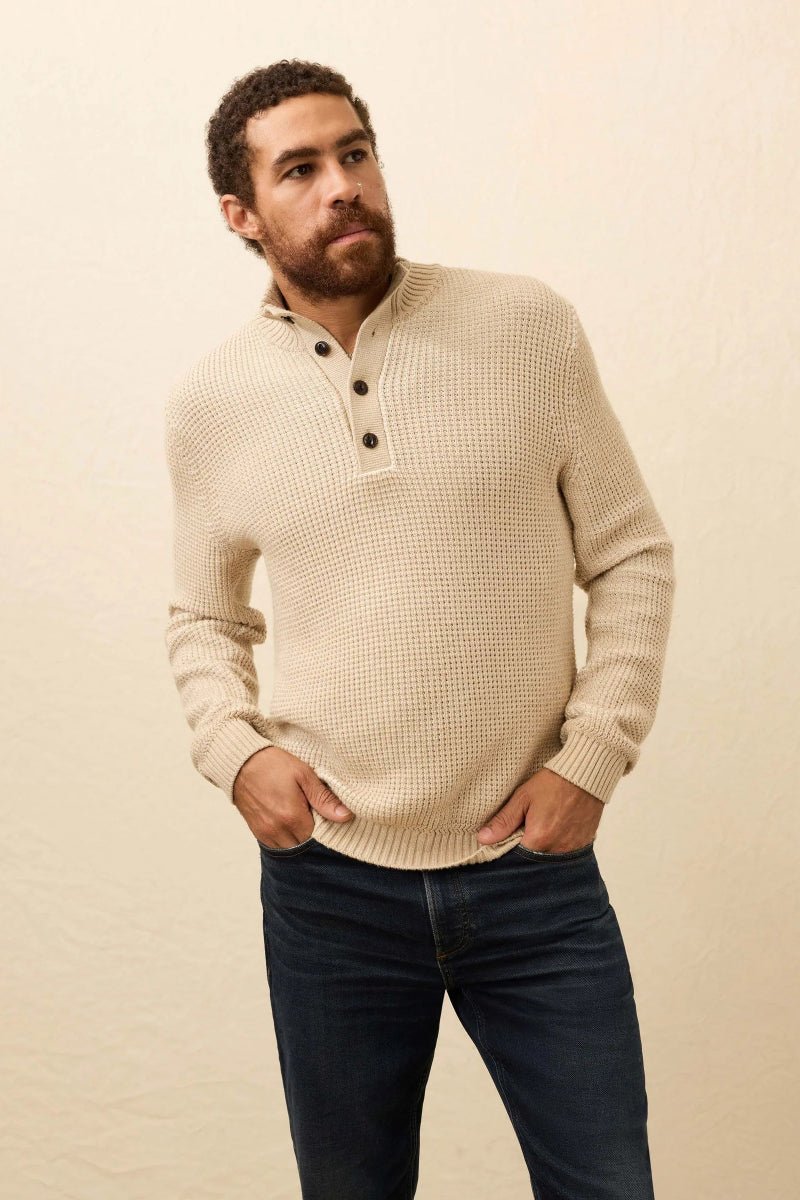 Man wearing a beige sweater with black buttons against a beige background