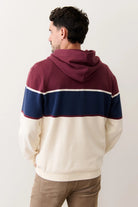 Man wearing a color-blocked hoodie with maroon, navy, and beige sections on a plain background.