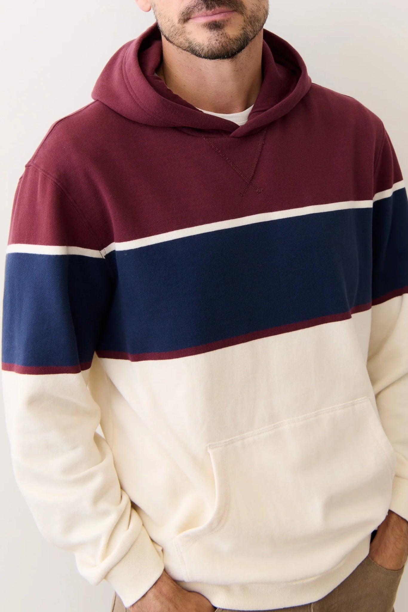 Person wearing a maroon, navy, and cream color-blocked hoodie against a plain background