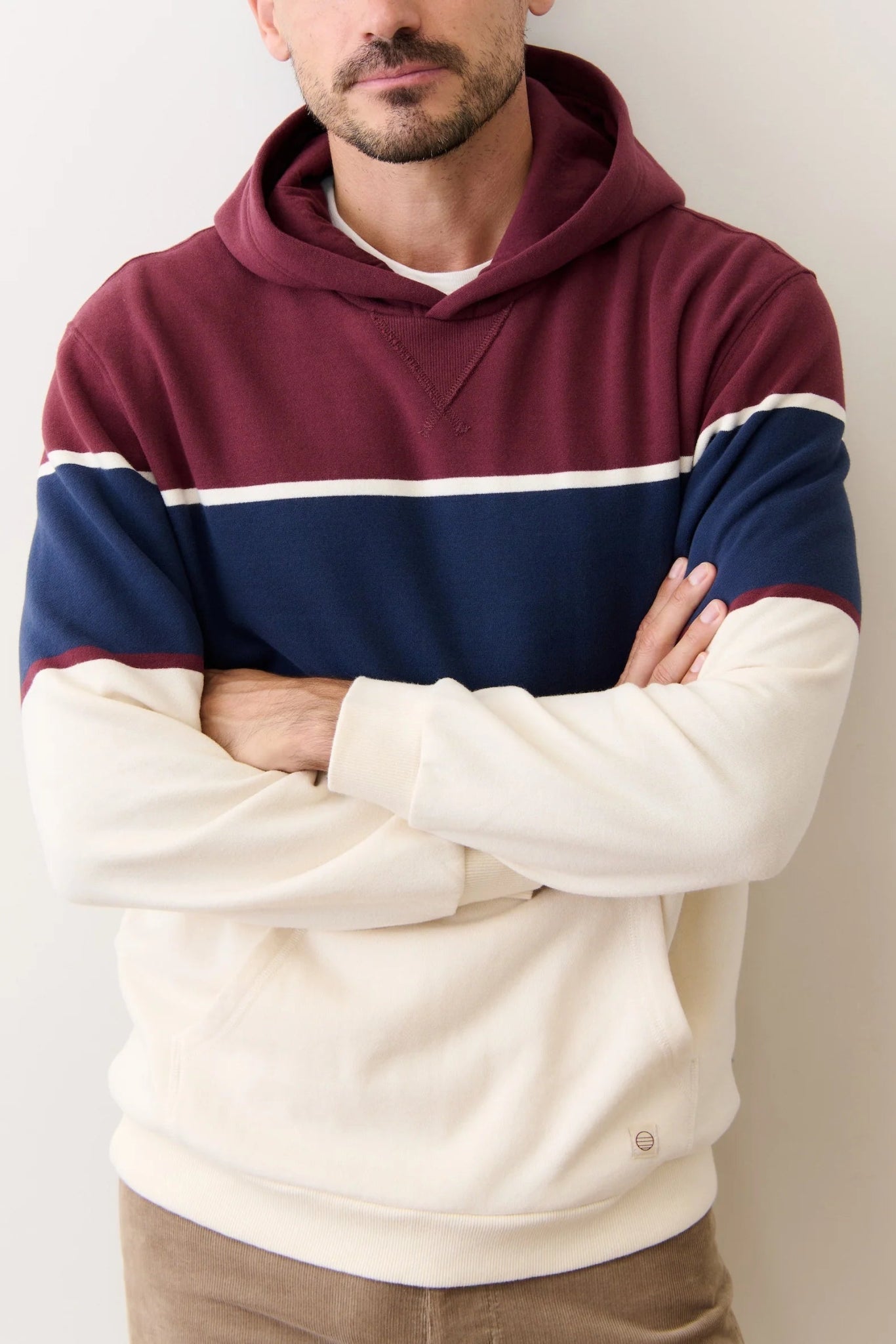 Person wearing a maroon, navy, and beige striped hoodie with arms crossed against a plain background