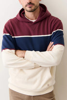 Person wearing a maroon, navy, and beige striped hoodie with arms crossed against a plain background