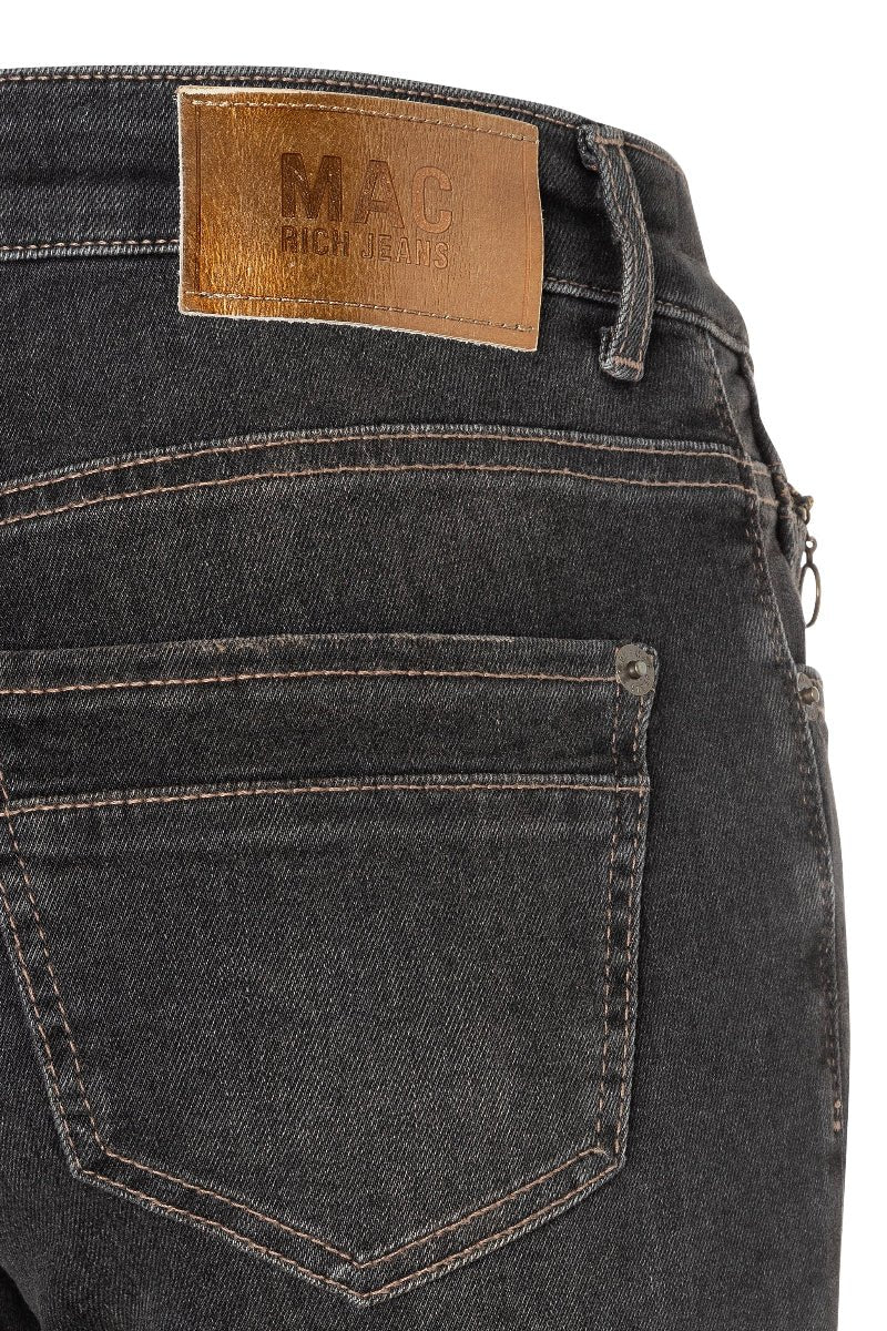 Close-up of dark denim jeans with a visible brand label on a white background