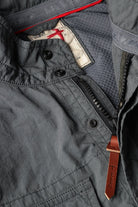 Close-up of a gray jacket with buttons and a leather strap, featuring a brand logo.