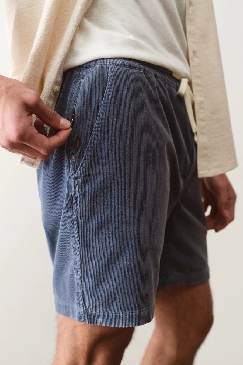 Person wearing blue shorts and a beige jacket on a plain background