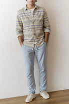 Person wearing a plaid shirt and light blue jeans against a white wall.