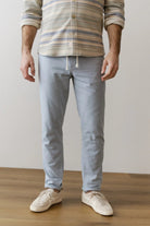 Person wearing a striped shirt and light blue pants on a wooden floor.