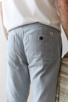 Person wearing light blue pants holding a striped jacket against a plain background