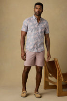 Man wearing a floral shirt and shorts standing against a beige background