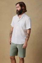 Man wearing a white short-sleeve shirt and green shorts against a beige background